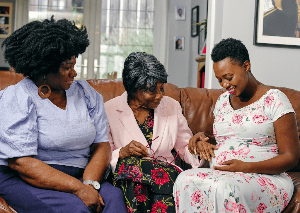 Pregnant woman sitting on sofa with female family member and community health worker