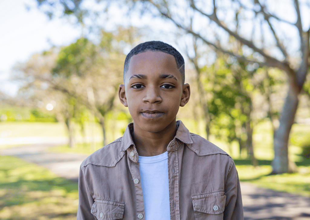 Young black boy looking at the camera while standing in a park. 