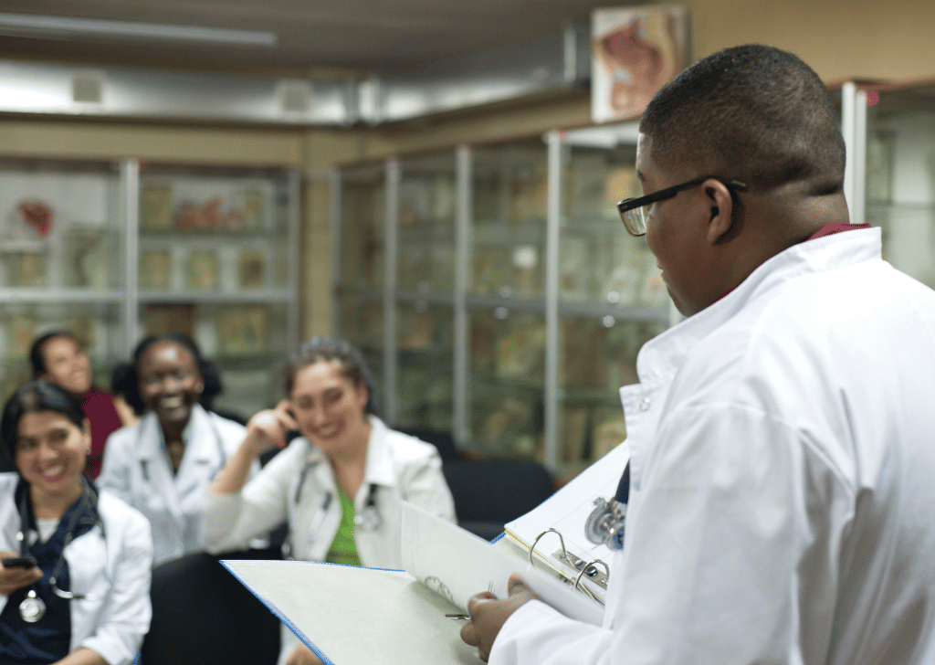 medical teacher, conducts a lesson for medical students. A group of young people of different gender, mixed races, sit on chairs in the classroom