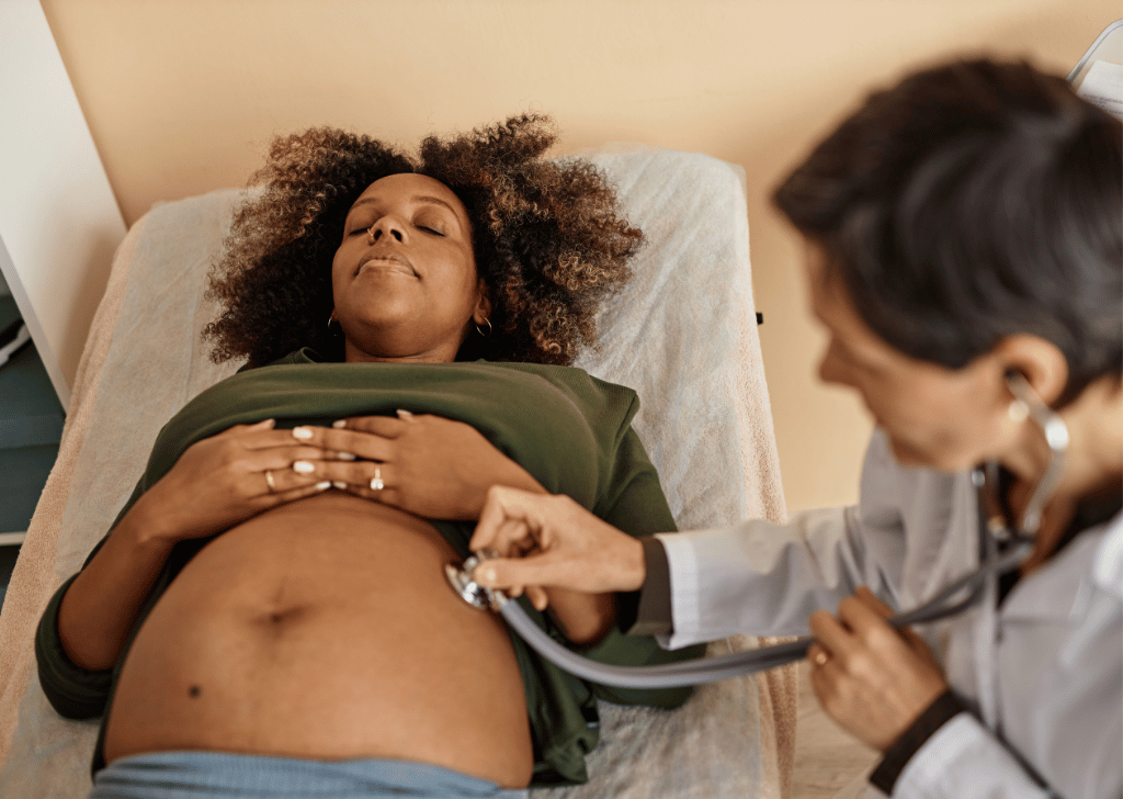 Black Pregnant Woman with Afro Exposing Belly Being Auscultated