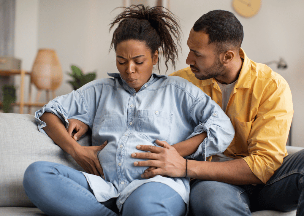 Pregnant African Woman Having Labor Pains, Husband Hugging Her Indoors