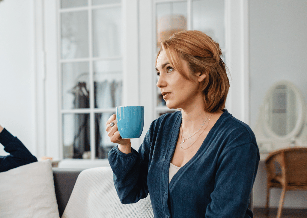 White woman sitting on a sofa holding a mug.