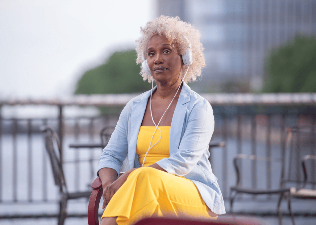 Middle age Black woman sitting on a public bench listening to headphones.